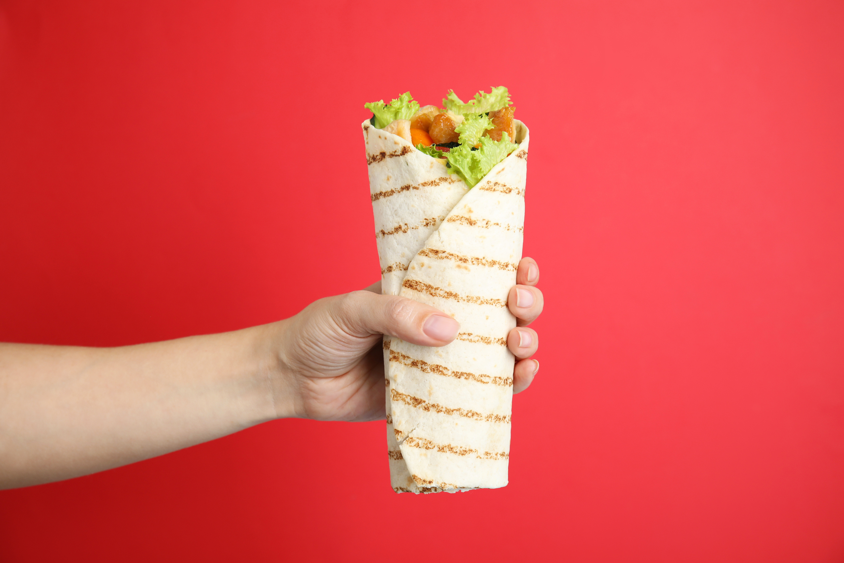Woman Holding Delicious Chicken Shawarma on Red Background, Clos